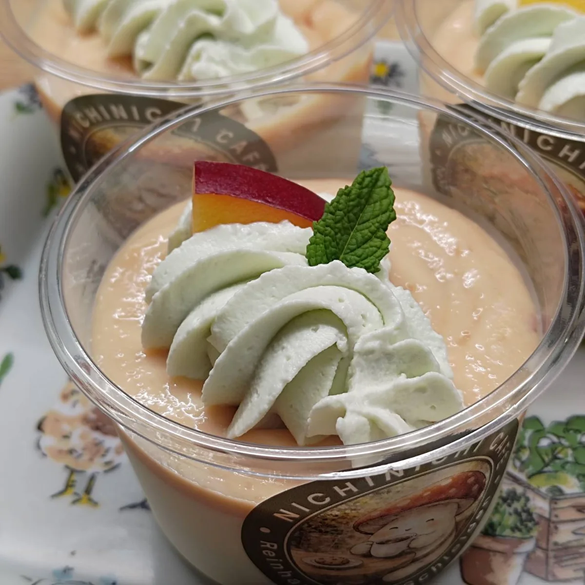 Pfirsich-Panna-cotta mit heller Creme, Pfirsichspalte und Minze im Becher